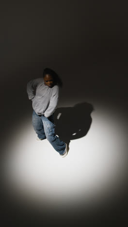 Vertical-Video-Full-Length-Studio-Portrait-Shot-Of-Young-Woman-Wearing-Hoodie-Dancing-In-Spotlight-With-Shadow-2